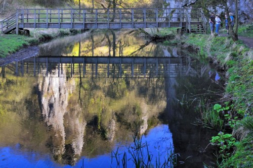 PIckering Tor and footbridge reflected in the calm waters of the River Dove